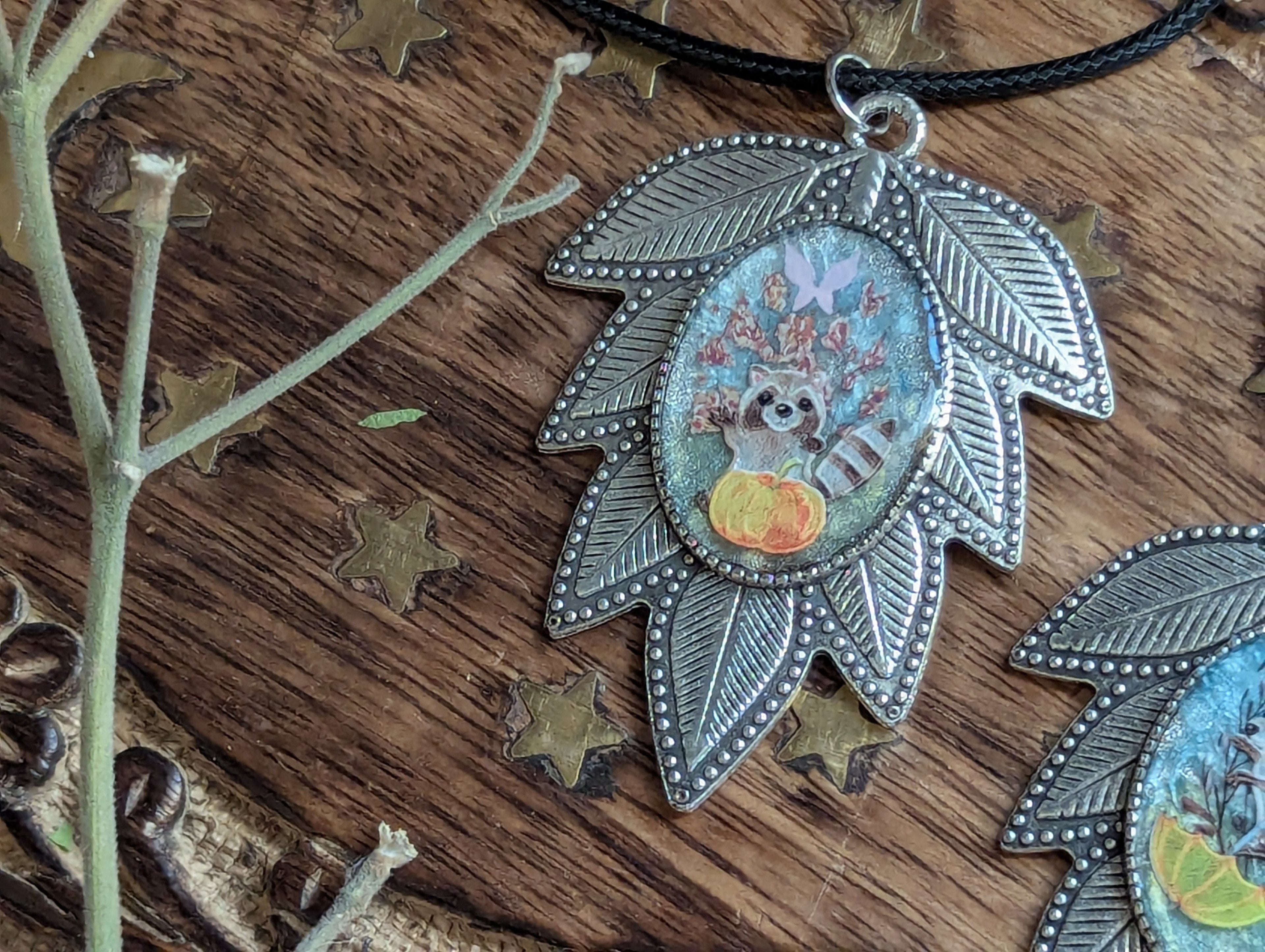 Whimsical raccoon pendant on black cord with botanical resin design