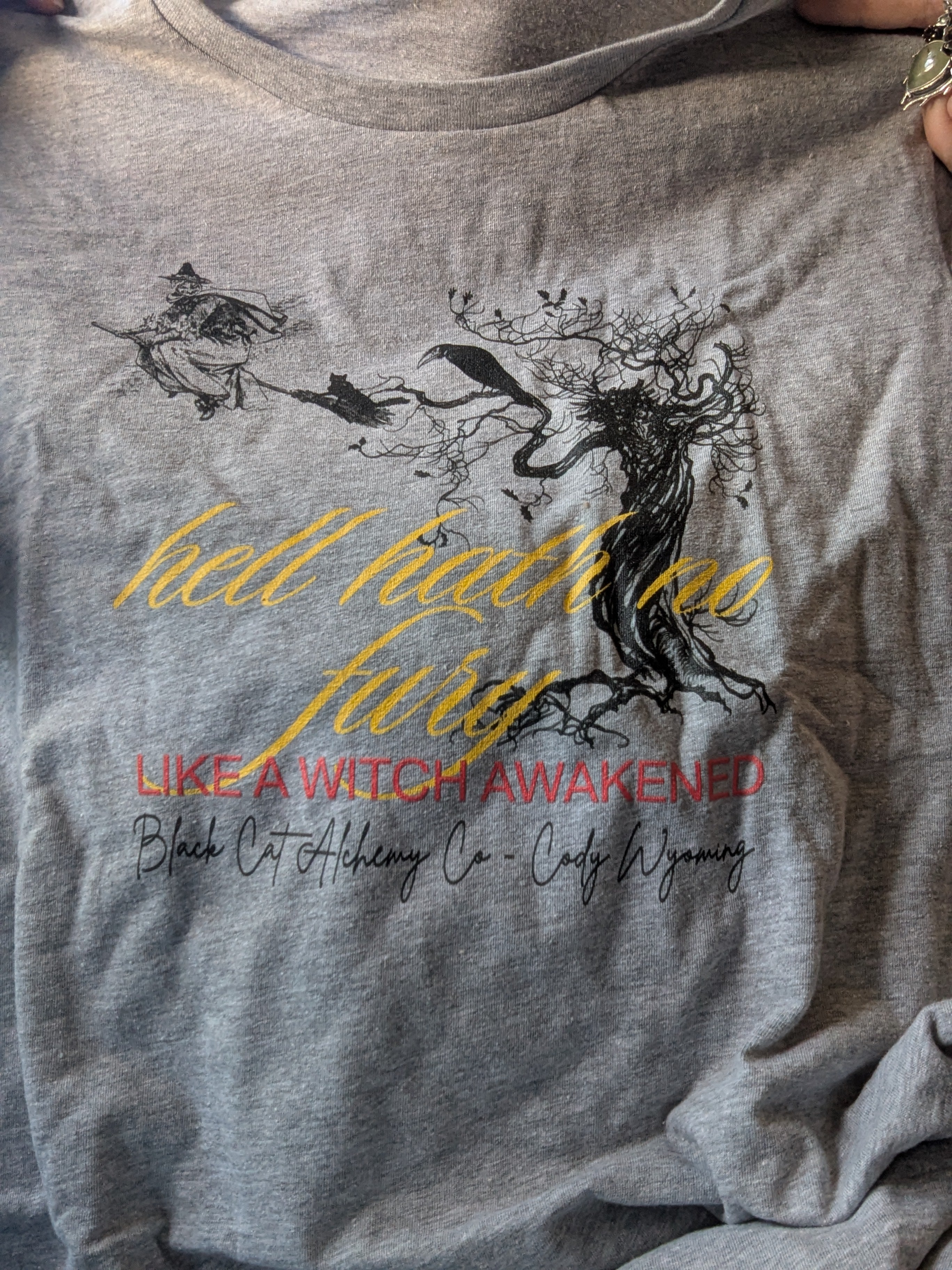 Grey t-shirt featuring the phrase "hell hath no fury like a witch Awakened" in an exclusive Black Cat Alchemy Company witchy design.